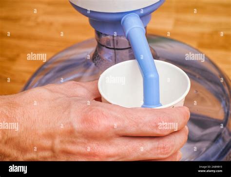 Woman Hand Pouring Water In Paper Cup From Bottle With Water Pump