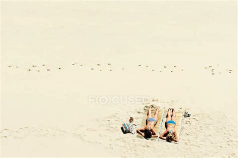 Две девушки загорают на песчаном пляже путешествия назначения лицом вниз Stock Photo