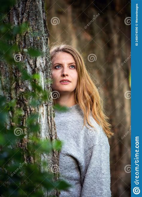Portrait Of Blond Woman Standing Between Trees Outdoors Stock Photo