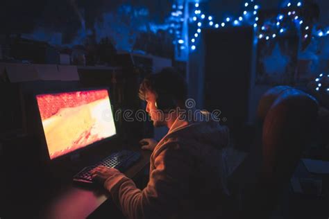 Focused Gamer Sits At The Computer At Home In The Cozy Room And Plays
