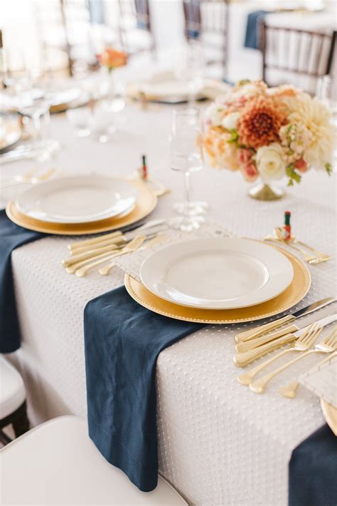 Guests Sat Along Long Tables Set With White Linens Embroidered With A