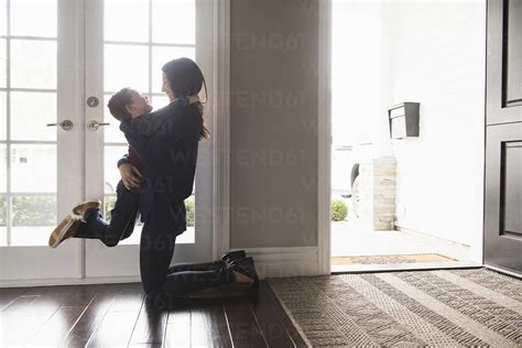 Mother Kneeling And Hugging Son In Living Room Stock Photo
