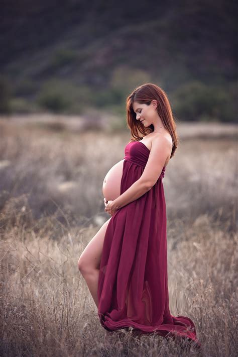 A Pregnant Woman In A Red Dress Poses For The Camera While Standing In