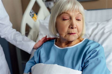 Female Doctor Consoling Upset Senior Woman With Grey Hair Lying In