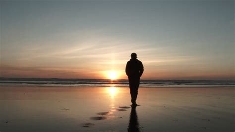 Man Walking Away On Sandy Beach To The Pacific Ocean In