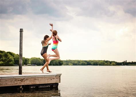 Two Young Girls In Swimsuits Jumping Off A Dock Into A Lake Photograph By Cavan Images Fine
