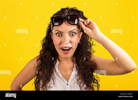 super amazed and stunned woman taking off sunglasses and looking at camera on vivid yellow