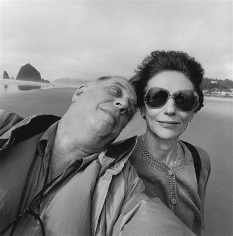 An Older Man And Woman Taking A Selfie On The Beach With Rocks In The