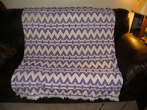 A Purple And White Blanket Sitting On Top Of A Brown Leather Couch Next