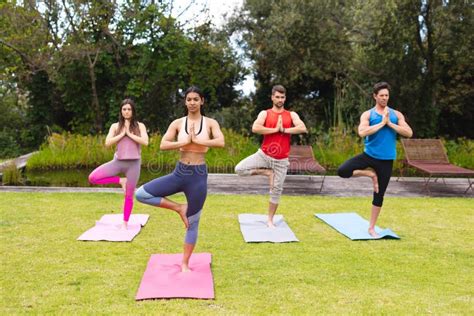 Female Instructor Teaching Tree Pose To Men And Woman On Exercise Mats During Yoga Session In