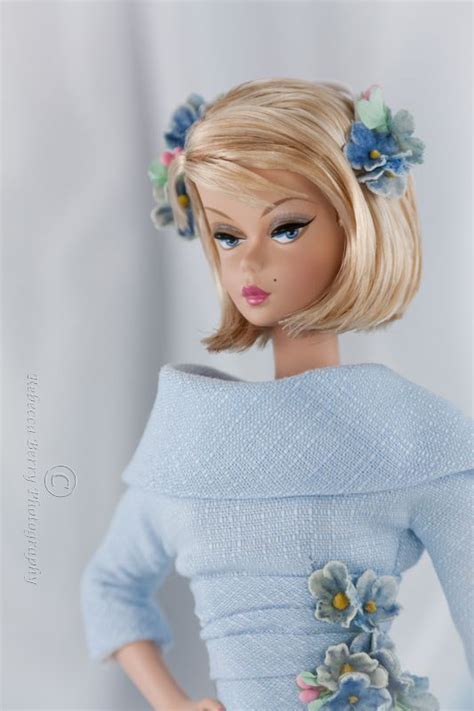 a doll with blonde hair wearing a blue dress and flowers in her hair is posing for the camera