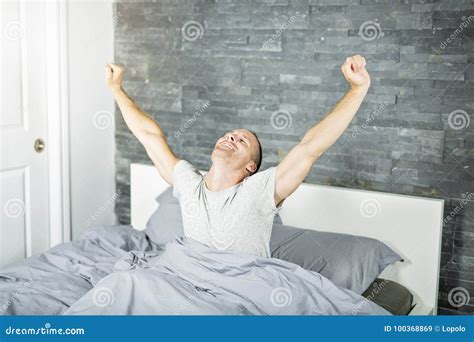 Cheerful Young Man Waking Up In Bed And Stretching His Arms Stock Image