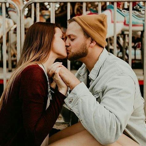 A Man And Woman Kissing In Front Of A Carousel