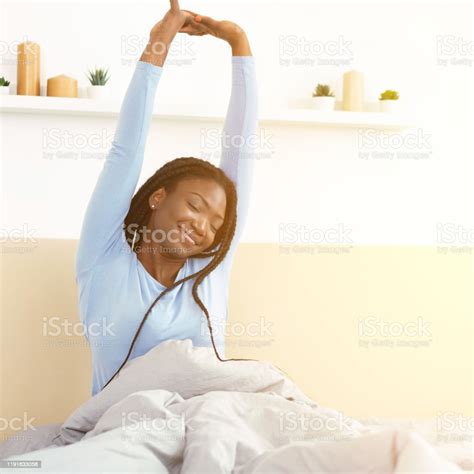 Happy Black Girl Waking Up Stretching Arms Sitting In Bedroom Stock