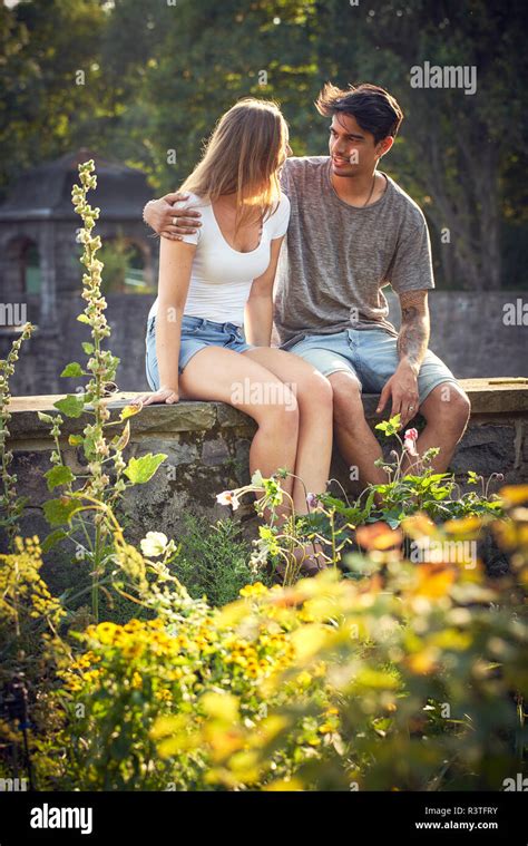romantische junge paare sitzen auf wand in einem park mit arme um stockfotografie alamy