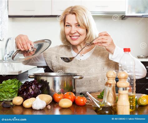 Mature Woman With Ladle Cooking Soup In Pan At Kitchen Stock Image