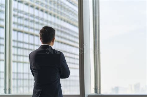 Asian Businessman Standing By Window Looking At View Stock Photo