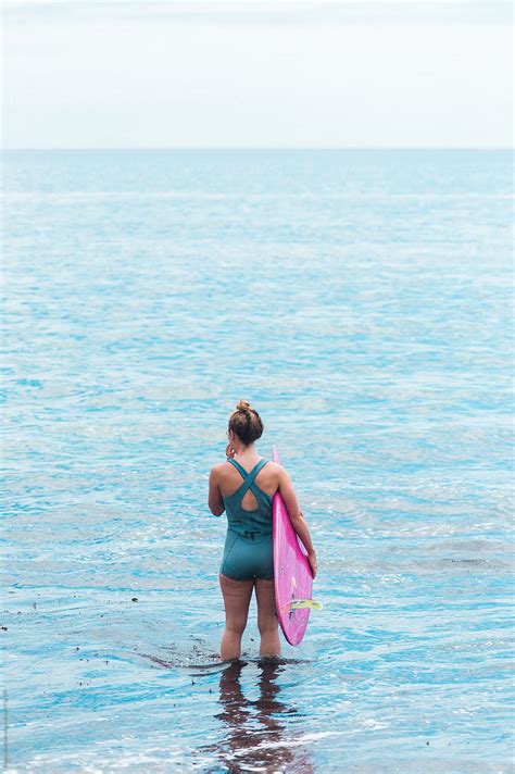 Woman Standing In The Ocean Holding A Surfboard Looking At The Horizon