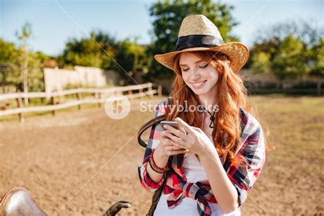 Smiling Happy Redhead Cowgirl Using Mobile Phone While Standing At