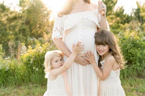 sisters touching mom s pregnant belly during a sunset maternity session in the field