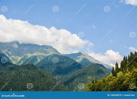 White Fluffy Clouds Float Above The Green Peaks Of The Mountains Stock