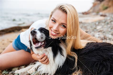 Cheerful Pretty Young Blonde Woman Sitting And Hugging Her Dog On The