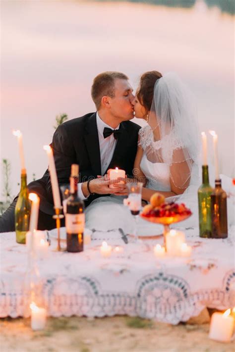 The Sitting Newlywed Couple Is Kissing Behind The Picnic Set Decorated
