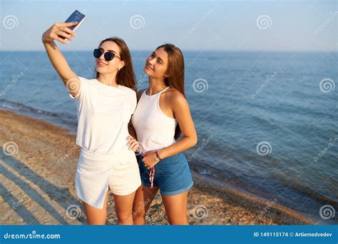 zwei junge frauen die ein selfie auf dem strand mit einer seeansicht nehmen freunde lcheln