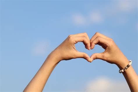 A Woman Raises Her Hand Above Her Head To Make A Heart Symbol On The Background Of The Bright