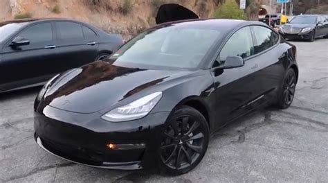 A Black Tesla Parked In A Parking Lot Next To Other Cars