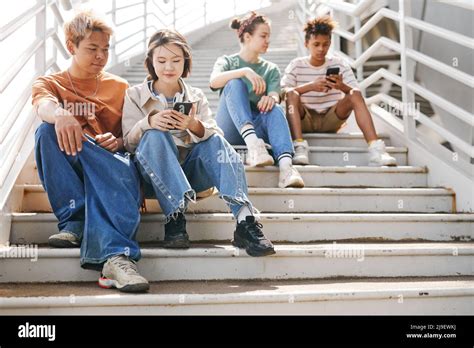 Airy Full Length Shot Of Diverse Teenagers Using Smartphones Outdoors