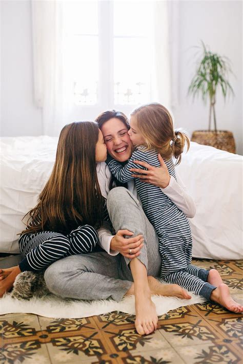 mom and her daughters kissing and hugging in the morning at home by stocksy contributor