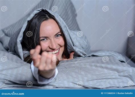An Attractive Smiling Woman Lying In Bed Under A Blanket Looking At