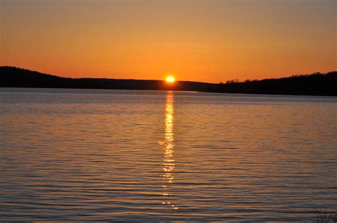 The Sun Is Setting Over Water With Hills In The Background