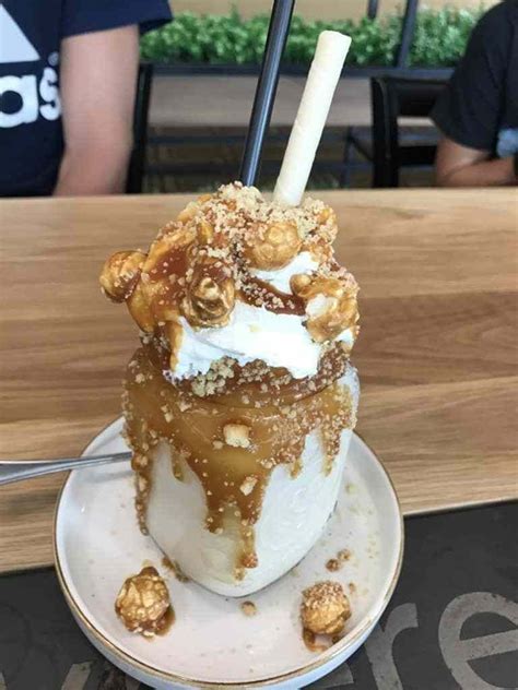 an ice cream sundae with walnuts on top sits on a plate at a table