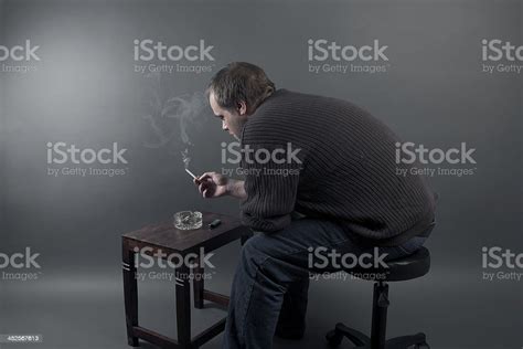 Depressed Young Man Sitting On A Chair Smoking Cigarette Stock Photo