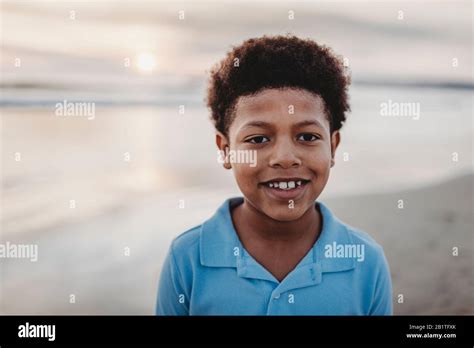 Portrait Of Young School Aged Boy Smiling At Beach During Sunset Stock