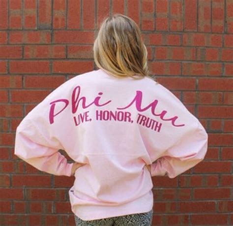 A Woman Standing In Front Of A Brick Wall Wearing A Pink Sweatshirt