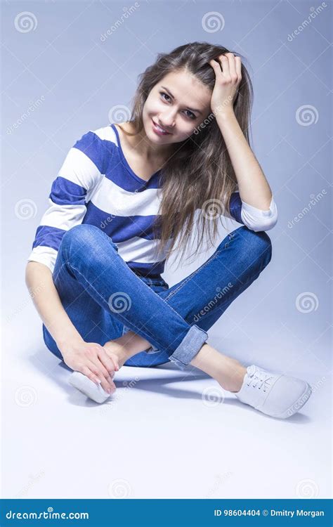 trendy and fashionable positive caucasian brunette girl sitting on floor with crossed legs stock