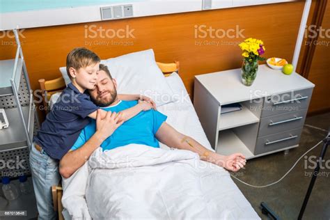 Father With Son Embracing While Laying On Hospital Bed At Ward Dad And