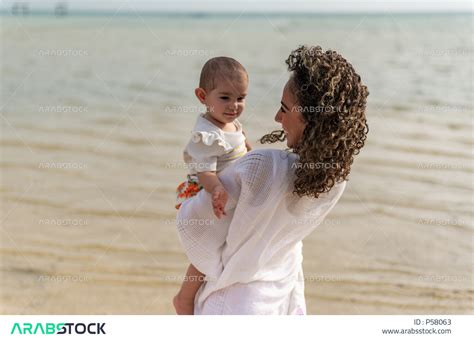 صورة مقربة لأم عربية خليجية سعودية تحمل إبنتها بحب وحنان، أم تلعب مع إبنتها بإيماءات وجه ويدين