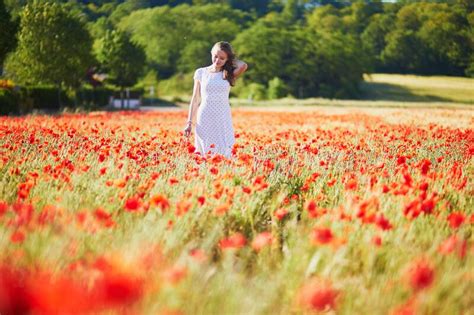 Beautiful Young Woman In White Dress Walking In Poppy Field On A Summer