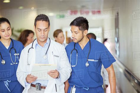 Doctor And Nurses Reading Medical Chart In Hospital Hallway Stock