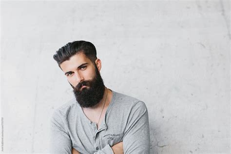 Young Man With Beard Leaning Against A Gray Wall By Stocksy