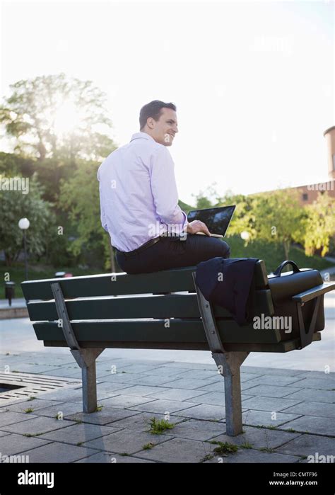 Smiling Businessman Sitting On Bench And Using Laptop Stock Photo
