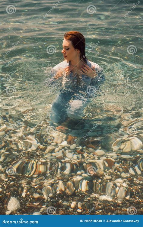 A Girl In A Shoulder Length Denim Jumpsuit Stands In Seawater Her Gaze