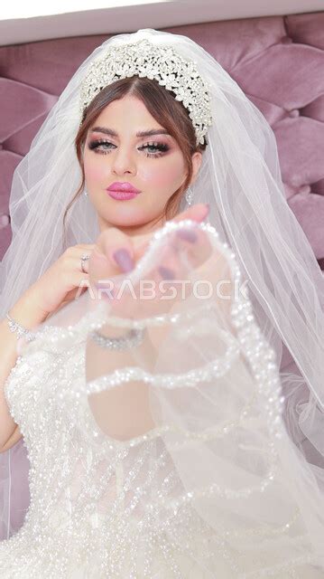 عروس عربية خليجية سعودية تقوم بجلسة تصوير ، مسكة عروس يوم زفافها ، بدلة زفاف بيضاء ، باقة ورود