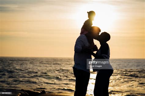 Silhouette Man Kissing Wife While Carrying Daughter On Shoulders At