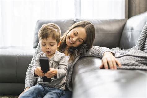 mother and her son are watching tv while sitting on a couch stock image image of technology