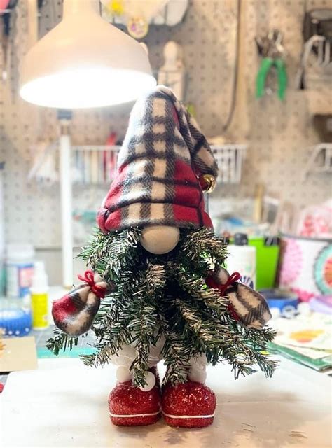 A Small Christmas Tree With Red Shoes And A Plaid Hat On It S Head